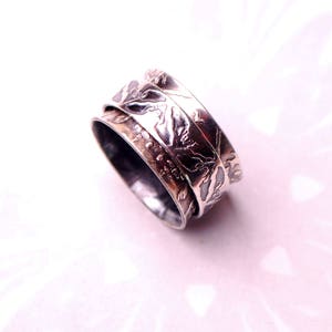 May include: A silver spinning ring with a textured design. The ring is made of two bands that spin independently.