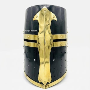 May include: A black and gold medieval crusader helmet. The helmet has a gold cross design on the front and gold trim. It features small ventilation holes and the text "Musigaa JAHAN®".