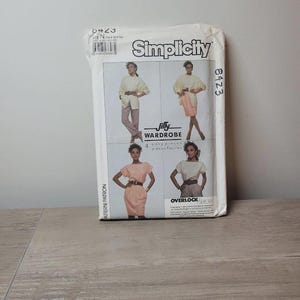 May include: A Simplicity 8423 sewing pattern envelope for a Jiffy Wardrobe. The white paper packaging features four photographs of garments including tops, skirts, and pants, with the text Simplicity, 8423, Jiffy Wardrobe, and Overlock printed on the front.