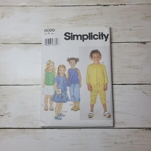 May include: A Simplicity sewing pattern featuring illustrations of children's clothing. The pattern includes a variety of outfits, such as dresses, tops, and pants. The pattern number is 9086, and the size is A 3-4. The cover is white with the Simplicity logo.