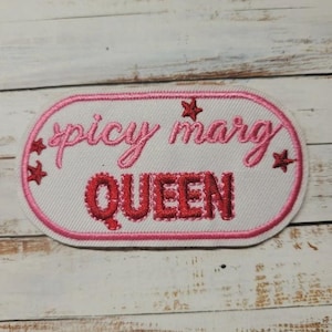 May include: An oval-shaped embroidered patch with a white background and a pink border. The text "spicy marg" is stitched in pink cursive, and the word "QUEEN" is stitched in bold red block letters. Small red stars are scattered around the text.