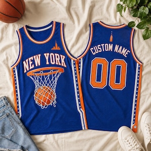 May include: A blue basketball jersey featuring the text NEW YORK and a graphic of a basketball in a hoop on the front. The back displays the text CUSTOM NAME and the number 00. The jersey has orange and white trim with star patterns on the sides.