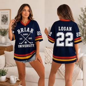 May include: A navy blue V-neck jersey with red and yellow stripes on the sleeves and hem. The front features the text BRIAR UNIVERSITY, HAWKS, EST. 2015, and a hockey graphic. The back displays the name LOGAN and the number 22 in white.
