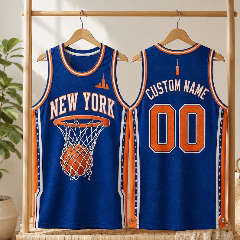 May include: A blue basketball jersey featuring the text NEW YORK and a basketball hoop graphic on the front. The back displays the text CUSTOM NAME and the number 00. The jersey has orange and white trim, side panels with star patterns, and a skyline icon.