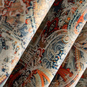 May include: Close-up of folded fabric with a detailed paisley pattern. The design features a mix of colours, including red, orange, blue, and beige. The fabric has a textured appearance, with visible folds and layers.