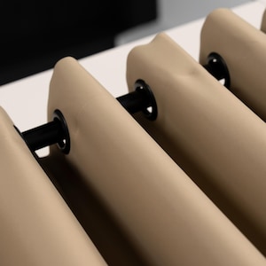 Könnte beinhalten: Nahaufnahme von beigefarbenen Vorhängen mit schwarzen Ösen und Stangen. Der Stoff ist glatt und hat eine einfarbige Farbe. Die Vorhänge sind teilweise geöffnet und geben einen Blick auf den Hintergrund frei.