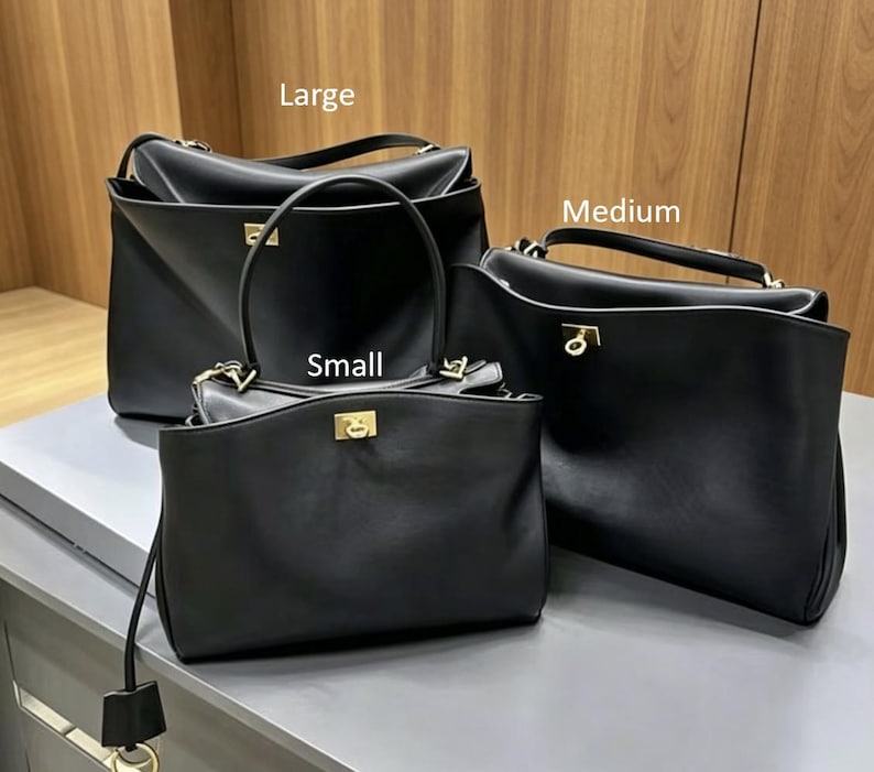 May include: Three black leather handbags of varying sizes: large, medium, and small. Each bag features a structured design with a top handle and a gold-colored clasp. The bags are displayed on a light gray surface.
