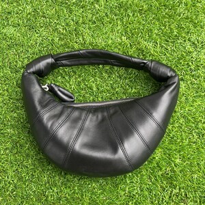 May include: A black crescent-shaped shoulder bag with a smooth finish, featuring a curved silhouette, a single integrated handle with knotted ends, and a silver-toned metal zipper closure along the top edge of the main compartment.