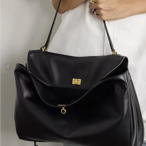 May include: Black leather handbag with a flap closure and gold-tone hardware. The bag has a structured design with a top handle and a long shoulder strap. The bag is a classic style, suitable for everyday use.