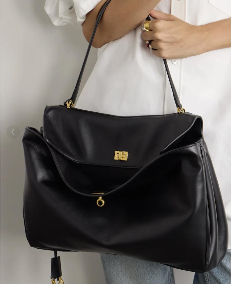 May include: Black leather handbag with a flap closure and gold-tone hardware. The bag has a structured design with a top handle and a long shoulder strap. The bag is a classic style, suitable for everyday use.