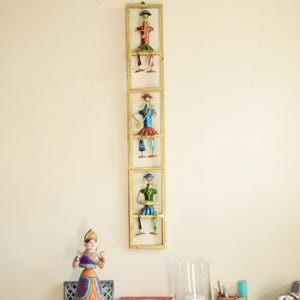 May include: A vertical gold-toned metal wall hanging featuring three stacked rectangular frames. Each frame contains a stylized metal figure in vibrant colors, including red, blue, and green, depicting musicians playing instruments.