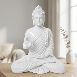 May include: A white Buddha statue in a seated lotus position with the right hand raised in a gesture of protection and the left hand resting on the lap. The figure features a textured ushnisha, elongated earlobes, and draped robes with folds.