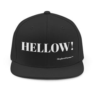 May include: A black snapback cap featuring the word HELLOW! in large white capital letters across the front panels. Below the main text, the words Shepherd Farms™ are printed in a smaller white font. The hat has a flat brim and a structured crown.
