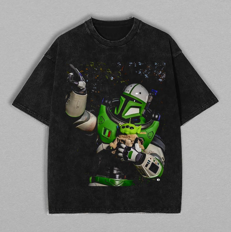 K&ouml;nnte beinhalten: Schwarzes T-Shirt mit einer Grafik eines gr&uuml;n-wei&szlig;en Weltraum-Rangers, der einen kleinen gr&uuml;nen Au&szlig;erirdischen h&auml;lt. Der Weltraum-Ranger tr&auml;gt einen gr&uuml;n-wei&szlig;en Anzug mit Helm. Der Au&szlig;erirdische ist in eine braune Decke geh&uuml;llt. Das T-Shirt hat einen verblichenen, Vintage-Look.