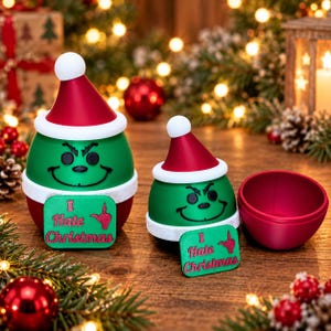 Könnte beinhalten: Zwei grüne, abgerundete Figuren mit roten Weihnachtsmützen mit weißem Rand. Jede Figur hat einen mürrischen Gesichtsausdruck und ein grünes Schild mit dem roten Text I Hate Christmas und einer Handgeste. Eine Figur ist geöffnet.