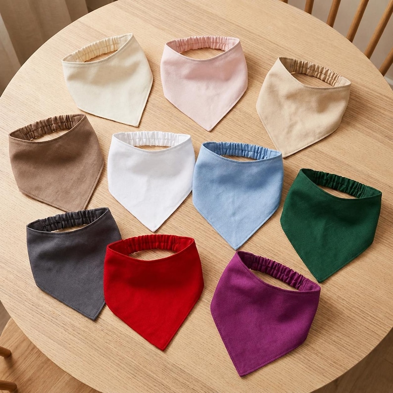 Pu&ograve; includere: Una collezione di dieci bavaglini triangolari in tessuto con fasce elastiche per il collo, disposti in un motivo circolare. I bavaglini sono disponibili in vari colori a tinta unita, tra cui bianco, crema, beige, marrone, grigio, rosso, rosa, azzurro, verde scuro e viola.