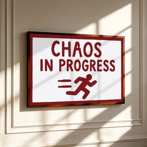 May include: A rectangular wall sign with a dark wood frame featuring a white background and dark red text that reads "CHAOS IN PROGRESS" above a dark red graphic of a stick figure running with horizontal motion lines behind it.