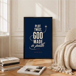 May include: A rectangular framed wall art print featuring a dark navy blue background with cream-colored text that reads: PLOT TWIST, GOD MADE a path, followed by the scripture reference ISAIAH 43:19, accented by a small star and curved lines.