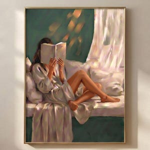 Emerald green wall art print in a thin gold frame on a warm white plaster wall above a herringbone wood floor, showing a brunette woman in a satin robe reading a book on a window seat with a sheer curtain and soft amber light.
