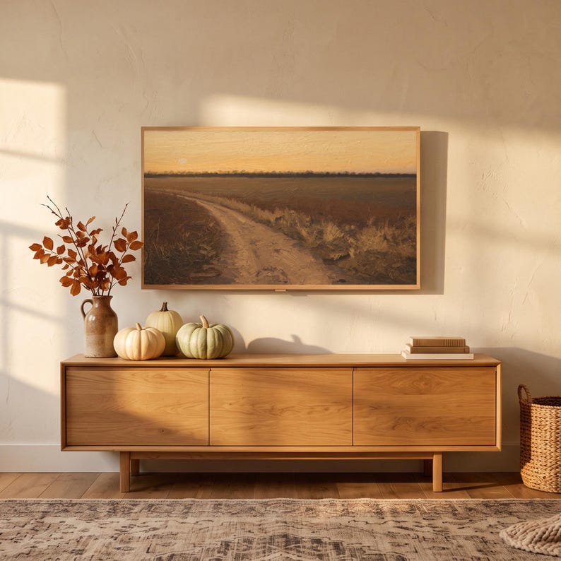 Autumn lane at dusk art from the set on a Frame TV in an autumn living room with window-pane sunlight, above an oak sideboard with pumpkins and rust leaves