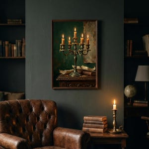 A walnut framed print of a lit brass candelabra hung on a dark green wall in a study, above a brown leather buttoned armchair with a stack of old books, a brass candlestick and a globe.