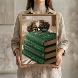 A person in a linen shirt holding the dog peeking over books art print in a slim gold frame against a soft neutral background