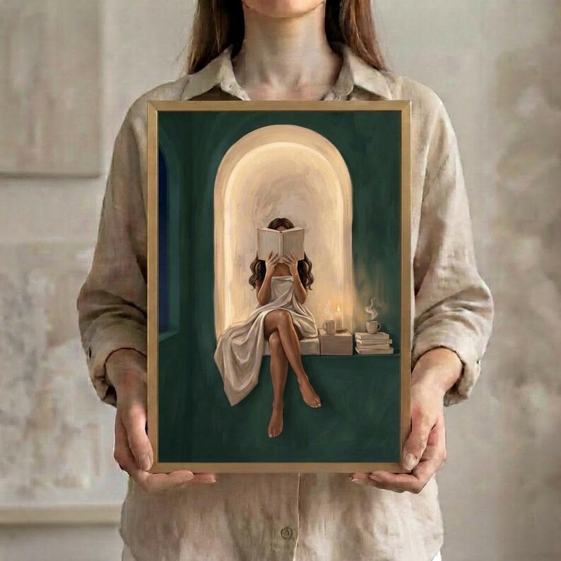 The brunette woman reading in an emerald green arched nook art print in a thin gold frame, held up in both hands to show its size.