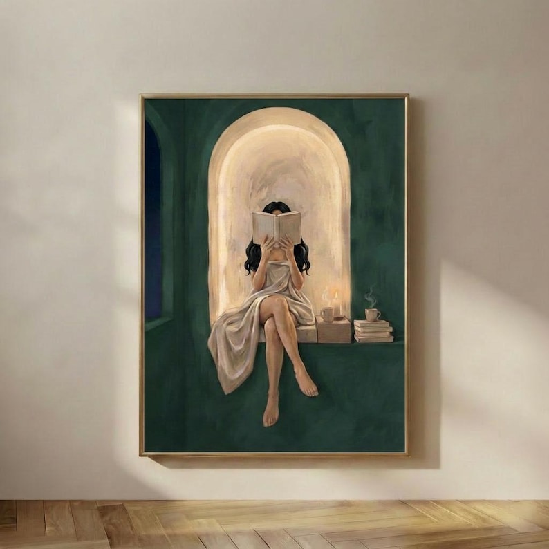 Emerald green reading nook art print of a woman with long dark hair reading by candlelight, in a thin gold frame on a plain plaster wall.