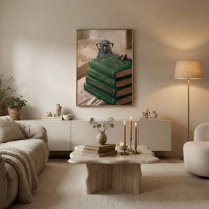 Wide view of a neutral living room with the pigeon peeking over books print framed above a low sofa in soft daylight