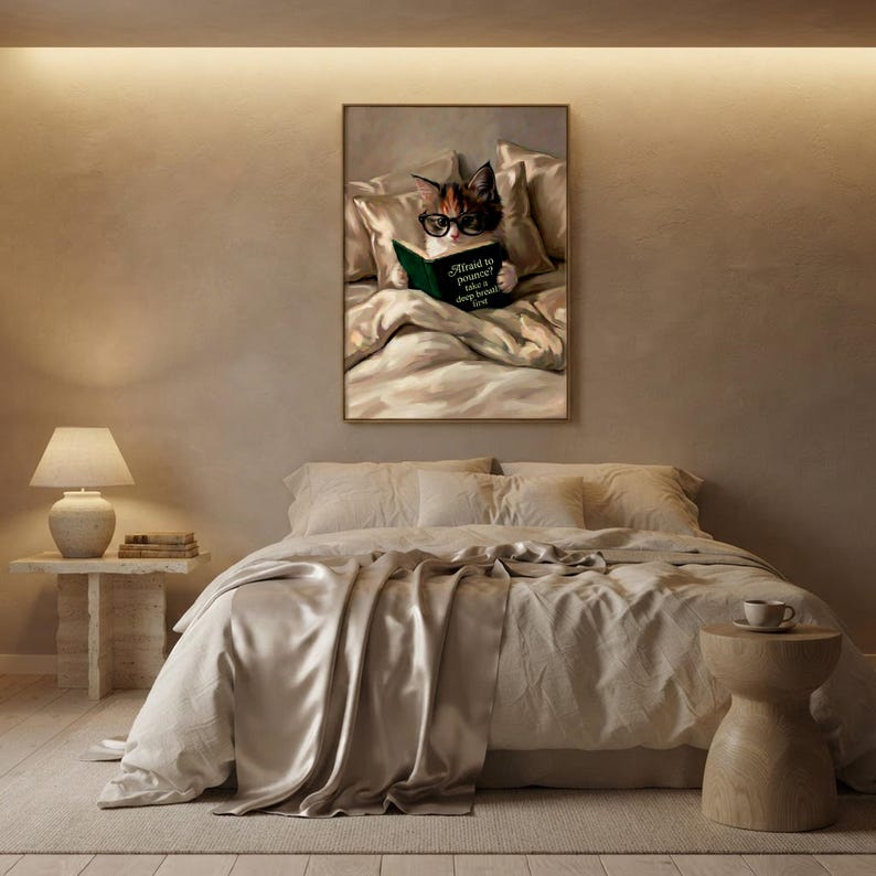 The framed kitten print on a warm plaster wall in a softly lit bedroom with linen bedding