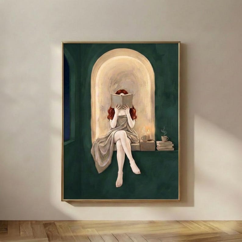 Emerald green reading nook art print of a redhead woman reading by candlelight, in a thin gold frame on a plain plaster wall.