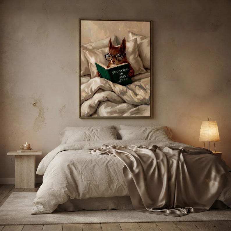 The framed squirrel print above a bed with layered linen and a satin throw, lit by a small lamp on a pale nightstand