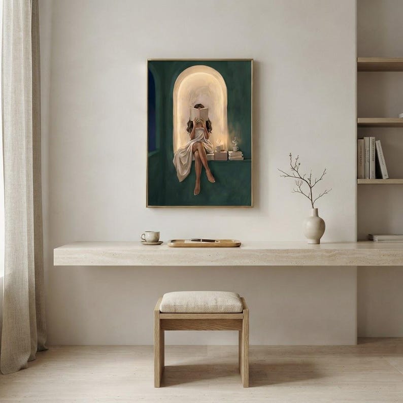 Emerald green reading nook art print on a pale plaster wall above a floating travertine desk with a coffee cup, a pen tray, a branch in a vase and an oak stool.
