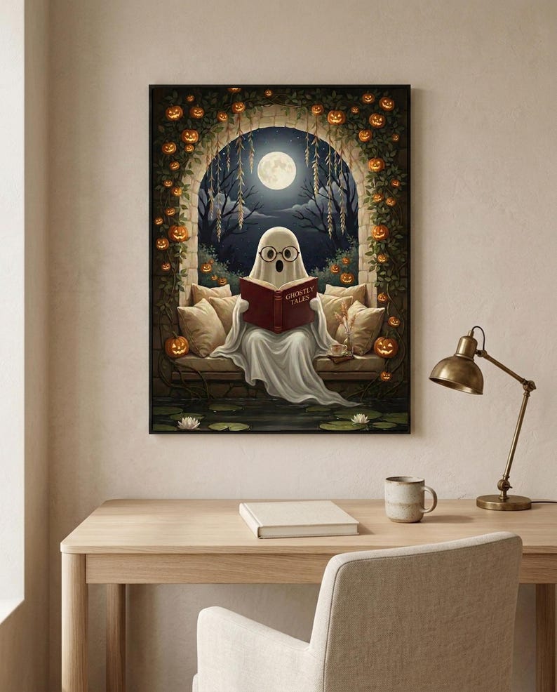 The pumpkin arch ghost reading print framed above a pale oak desk with a stoneware mug and a brass lamp