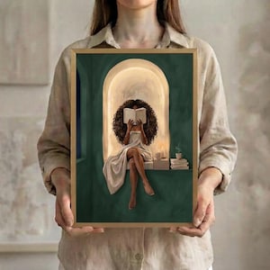 The emerald green arched nook art print of the Black woman with voluminous curls reading, in a thin gold frame, held up in both hands to show its size.