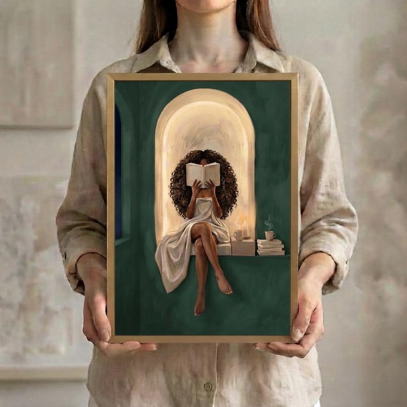 The emerald green arched nook art print of the Black woman with voluminous curls reading, in a thin gold frame, held up in both hands to show its size.