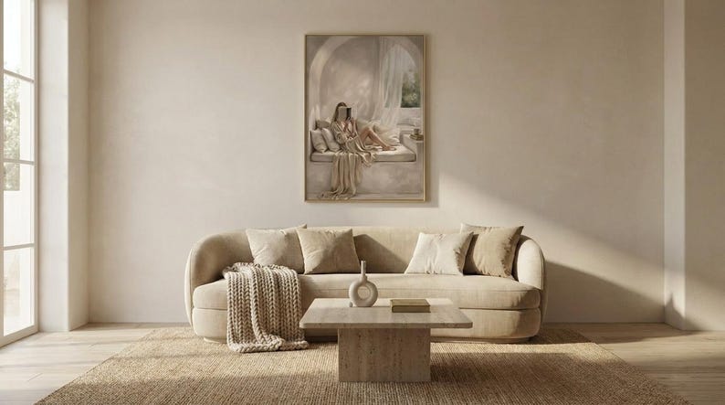 Wide living room view showing the woman reading nook wall art centered above a low sofa, gold frame, no mat.