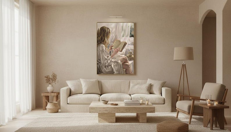Wide view of a neutral living room with the woman reading print framed in gold on a warm plaster wall between linen curtains