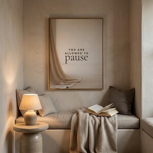 You Are Allowed to Pause styled in a cozy neutral reading corner, hung in a thin gold frame with no mat. neutral printable wall art, minimalist home decor, Japandi style, calm living room decor, slow living digital download.