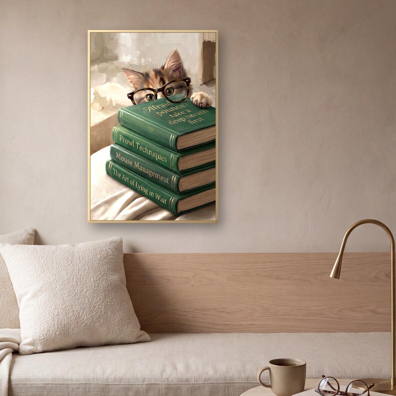 The framed cat peeking over books print above a low bench with a pale oak back panel, a bouclé cushion and a linen seat, beside a brass arc lamp and a small table holding a mug and a pair of reading glasses.