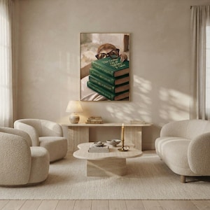 Sloth peeking over books wall art framed on a warm plaster wall in a calm light-filled living room with a cream linen sofa