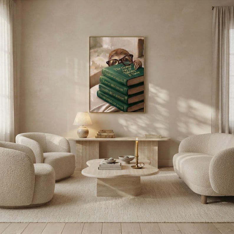 Sloth peeking over books wall art framed on a warm plaster wall in a calm light-filled living room with a cream linen sofa