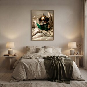 The dog reading print framed above a bed with linen bedding and an olive throw, between two matching bedside lamps