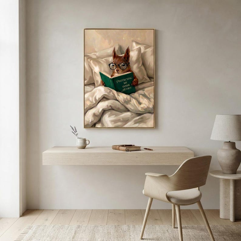 The squirrel reading print framed above a floating desk with a moulded chair, a mug and a ceramic lamp in a bright minimal workspace