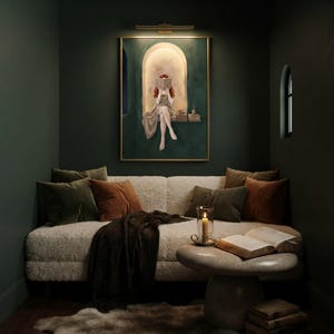 Emerald green reading nook art print lit by a brass picture light in a dark green reading alcove, above a sheepskin daybed with velvet and rust cushions, a candle and an open book.