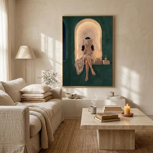 Emerald green reading nook art print in a thin gold frame on a sunlit plaster wall above a cream linen sofa, with a jute rug, a travertine coffee table, a lit candle and stacked books.