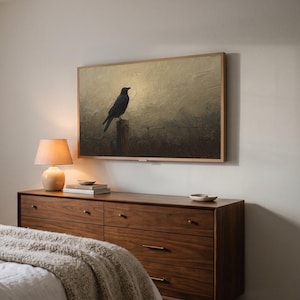 Crow on a fence art from the set on a Frame TV in a bedroom seen at an angle, above a walnut dresser with a lit lamp and a knit throw on the bed