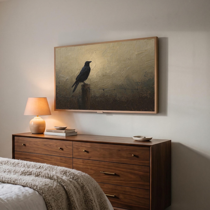 Crow on a fence art from the set on a Frame TV in a bedroom seen at an angle, above a walnut dresser with a lit lamp and a knit throw on the bed