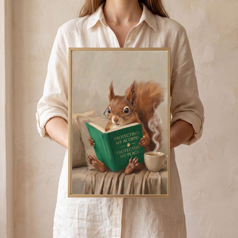 A person in a cream linen shirt holding the squirrel print in a slim gold frame against a plaster wall, showing the scale of one print from the set