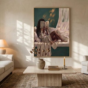 Gold-framed emerald green art print of a Black woman reading on a window seat in a sunlit living room with a linen sofa and armchair, shown wide to give a sense of scale.